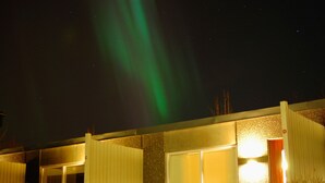 Een gebouw met grote ramen en een deur, onder een nachthemel met groene poollichten.