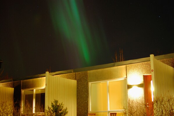 A building with large windows and a door, under a night sky with green aurora lights.