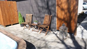 Een terras buiten met houten stoelen, een bijzettafeltje en een lantaarn.