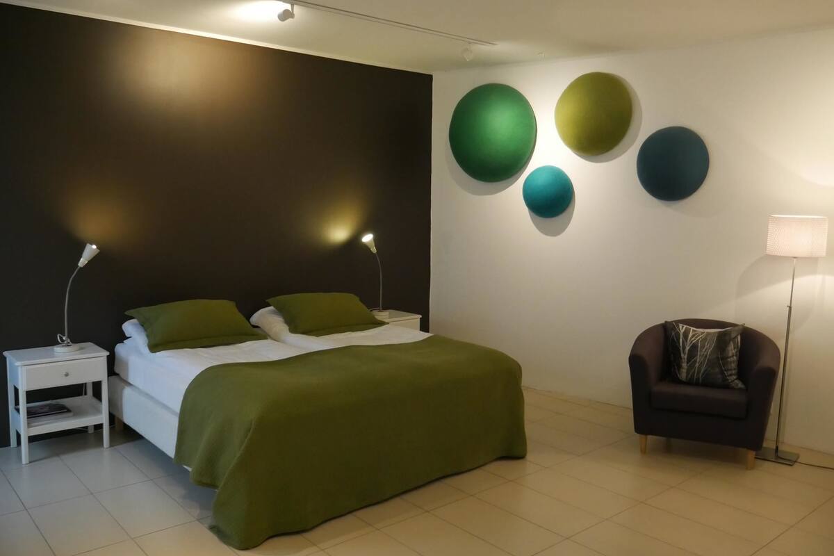 Un dormitorio moderno con cama, mesitas de noche, una silla y adornos en la pared.