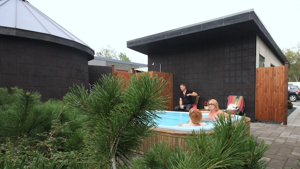 Een bubbelbad in een achtertuin met een houten terras en pijnbomen.