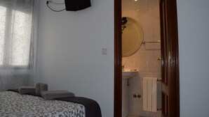 A bedroom with a bed, a bedside table, a wall-mounted TV, and a bathroom with a sink and shower. - Hostal Rofer (Madrid)