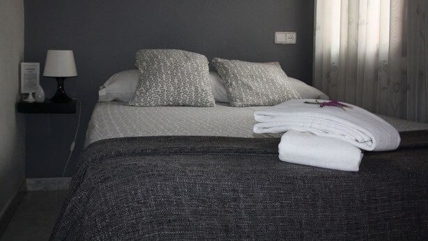 A neatly made bed with patterned pillows, a bedside lamp, and a power outlet on the wall. - Hostal Rofer (Madrid)