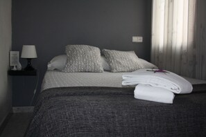 A neatly made bed with patterned pillows, a bedside lamp, and a power outlet on the wall.