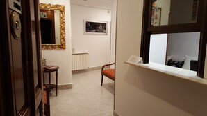 A hallway with a wooden door, a mirror, a framed picture, a chair, and a window with a view. - Hostal Rofer (Madrid)