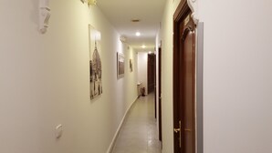 A hallway with white walls, a tiled floor, and several framed pictures. There is a door at the end of the hallway. - Hostal Rofer (Madrid)