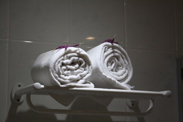 A towel rack with two rolled towels, each adorned with a purple flower.
