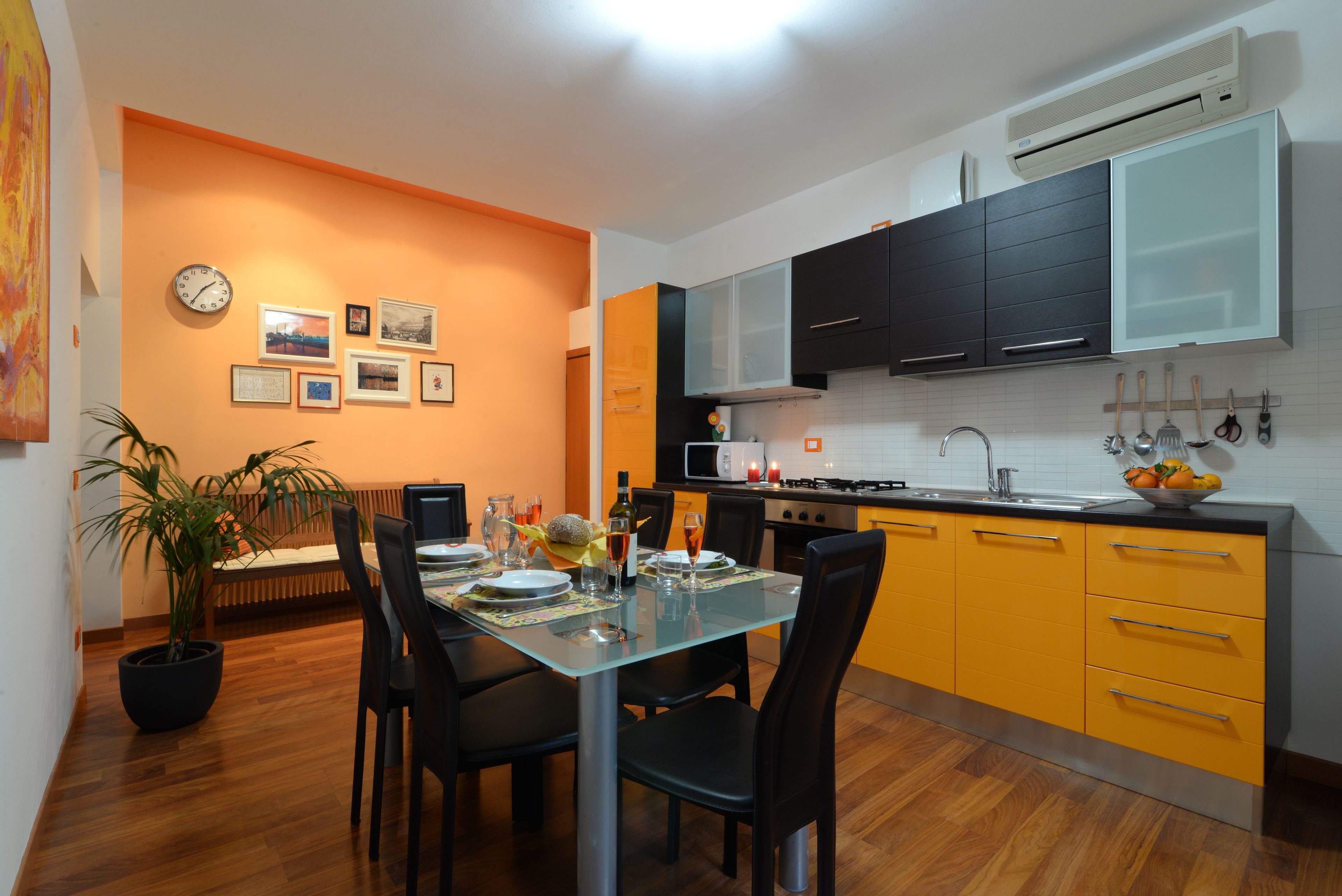 Une cuisine moderne avec des meubles de couleur orange, une table à manger pour quatre personnes et une horloge au mur.