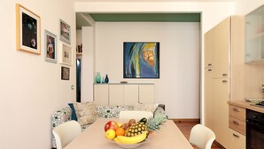 A dining area with a table set for two, a fruit bowl, a sofa with patterned cushions, and a kitchen area with cabinets and a stove. - Padovaresidence Piazza delle Erbe (Padova)