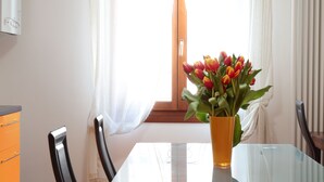 A dining area with a glass table, chairs, a vase with flowers, and a window with curtains. - Padovaresidence Piazza delle Erbe (Padova)