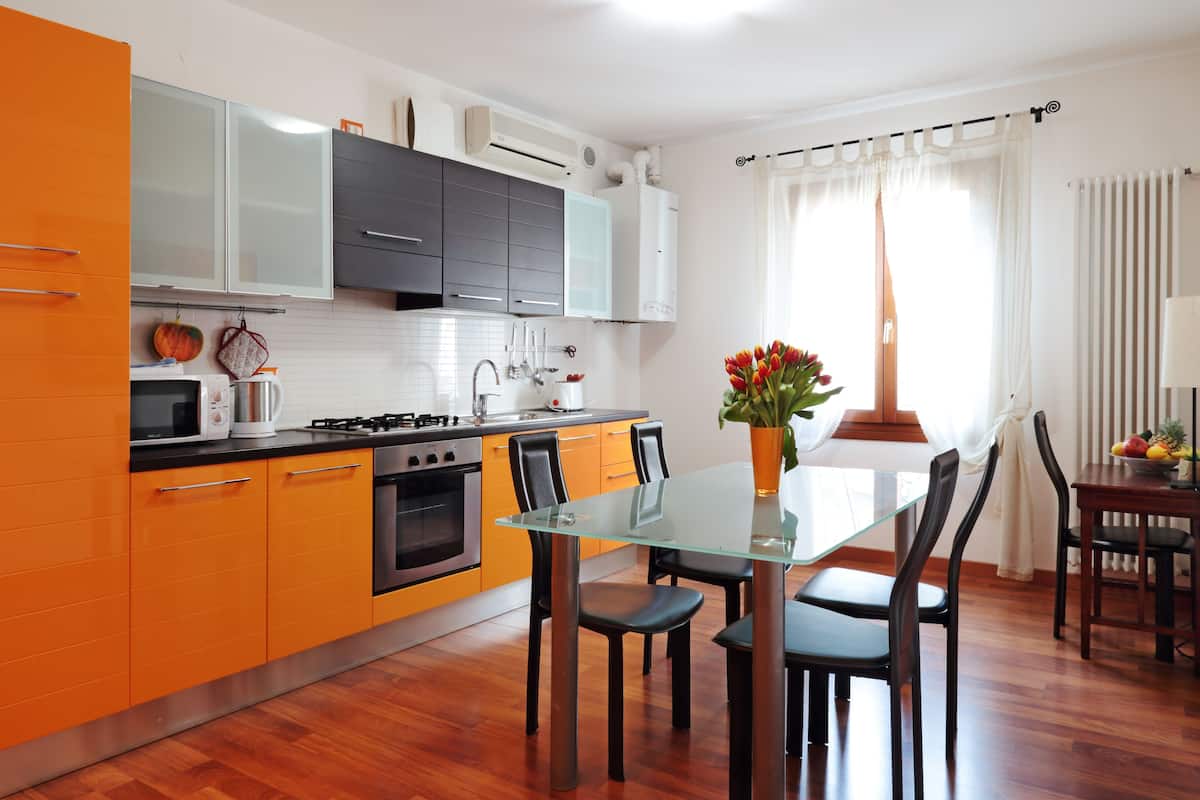 A modern kitchen with orange cabinets, a glass dining table, and a view of the outdoors.