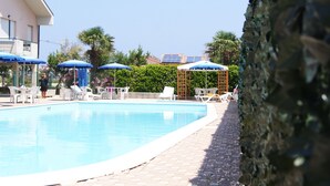 A swimming pool with lounge chairs and umbrellas, surrounded by greenery and a building with solar panels. - Polena Residence Hotel (Montenero di Bisaccia)