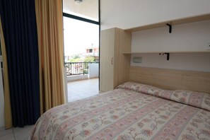 A bedroom with a bed, a wooden headboard, a window with curtains, and a balcony with a railing. - Polena Residence Hotel (Montenero di Bisaccia)
