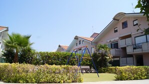A residential area with a playground, palm trees, and a building with balconies. - Polena Residence Hotel (Montenero di Bisaccia)