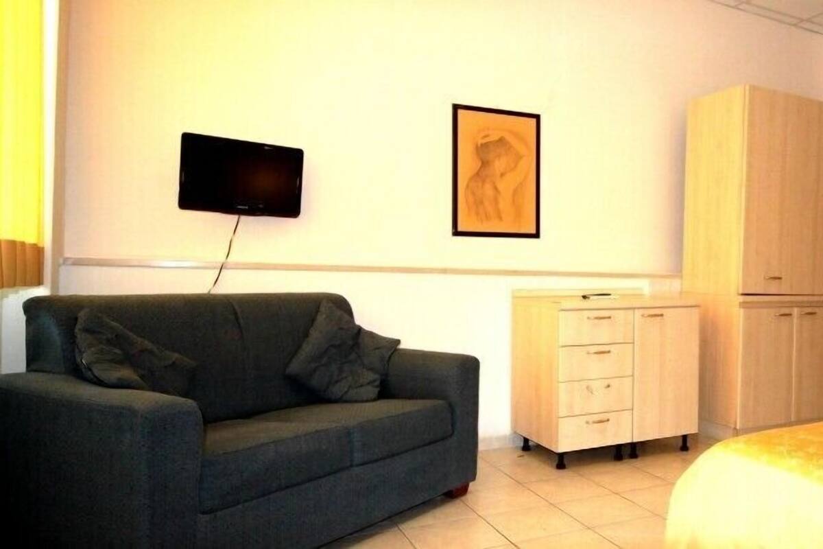 A room with a sofa, a bed, a TV mounted on the wall, a cabinet, and a door.