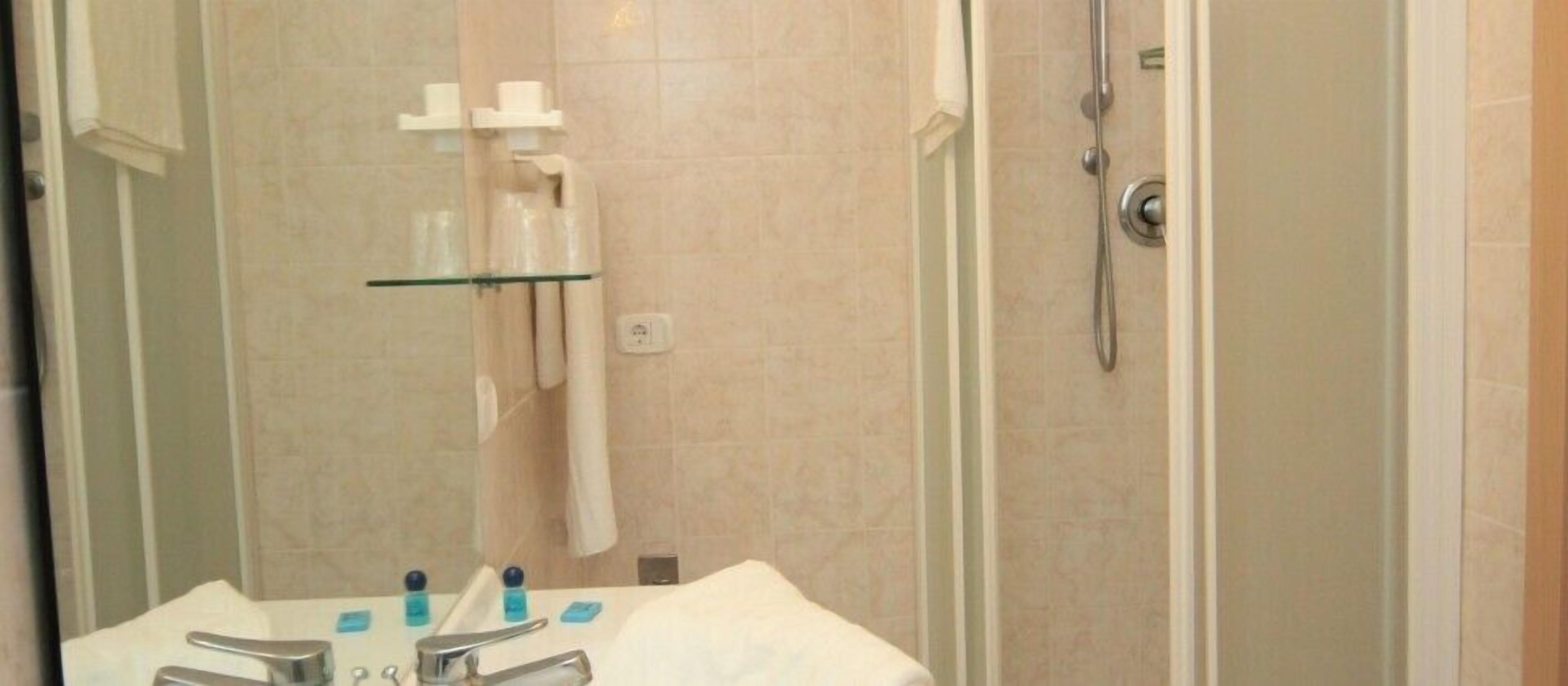 A bathroom with a glass shower enclosure, a sink with a mirror, and a towel rack.