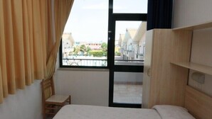 A bedroom with a bed, a wooden headboard, a small stool, and a window with curtains. - Polena Residence Hotel (Montenero di Bisaccia)