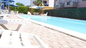 A pool area with white lounge chairs and umbrellas, a paved walkway, and a hedge. - Polena Residence Hotel (Montenero di Bisaccia)