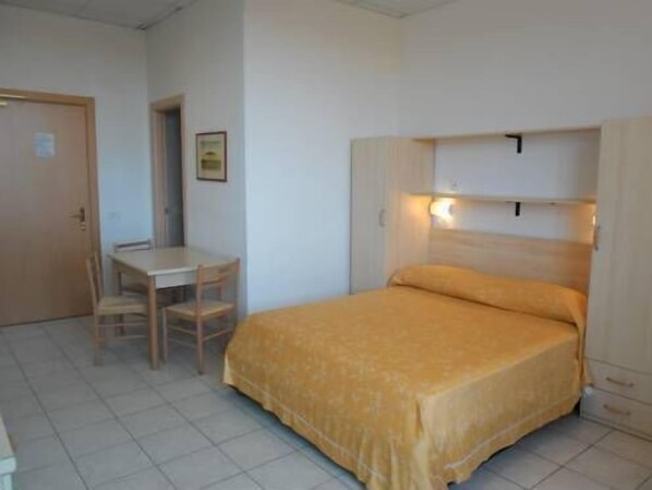 A small, single-bed room with a wooden bed frame, a bedside table, and a chair.