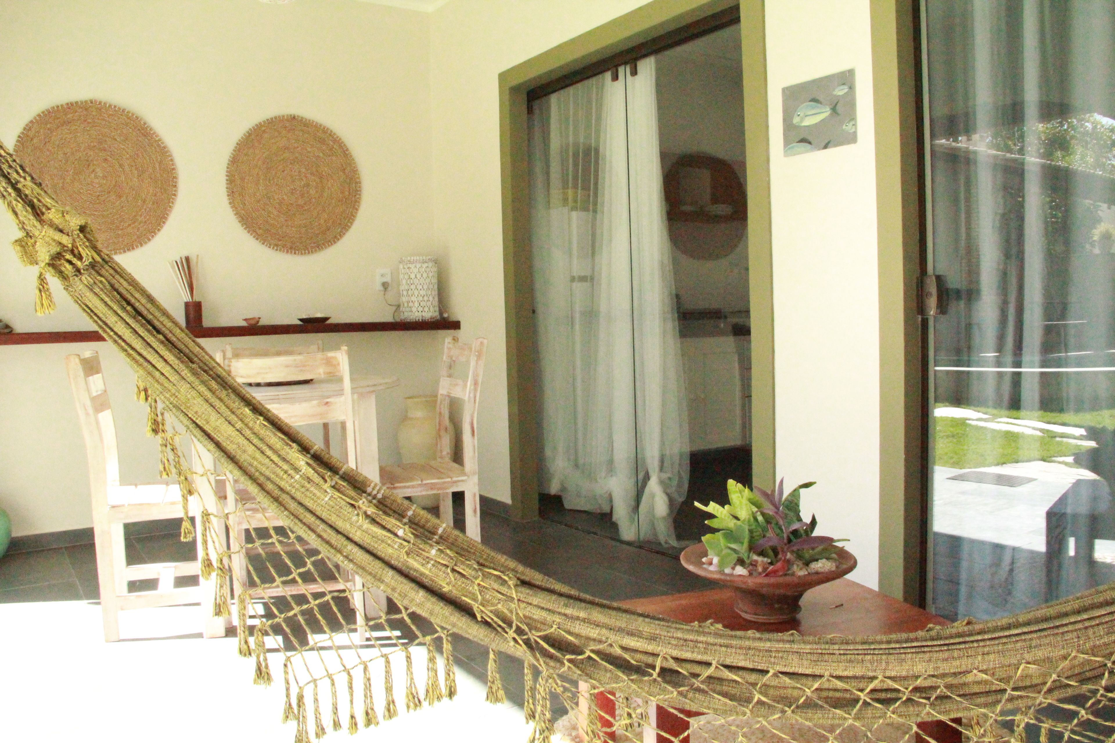 Un hamac sur une véranda, avec une plante en pot et une chaise en bois.