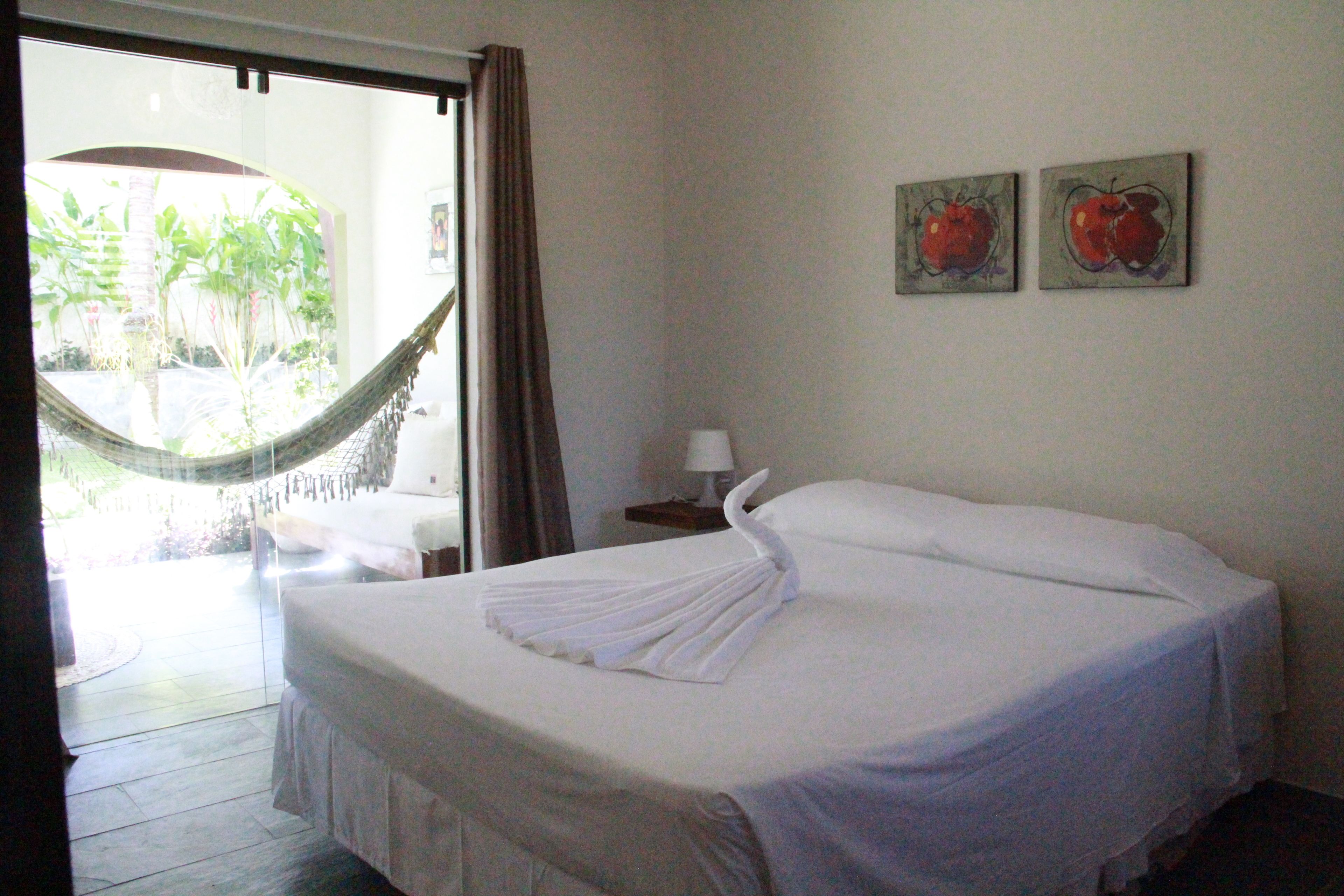 A hotel room with a bed, a nightstand, a lamp, and two fruit paintings on the wall.