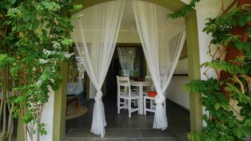 An arched doorway with white curtains, a white table with chairs, and green foliage.