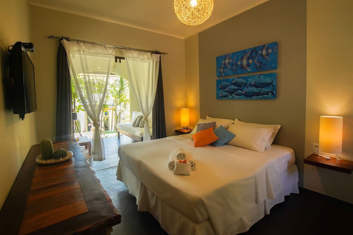 A hotel room with a bed, a wooden table with a cactus, a lamp, and artwork on the wall.