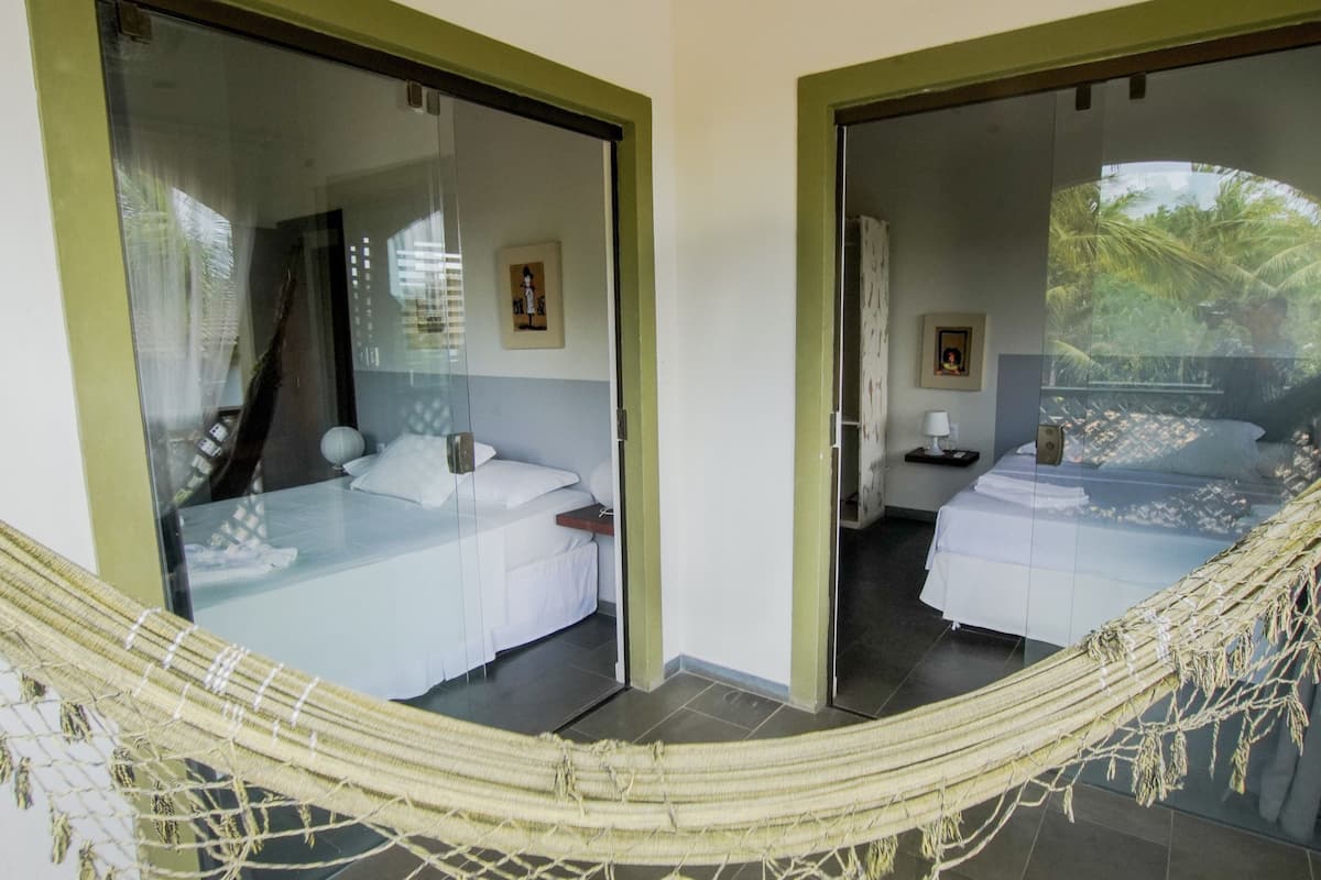 A room with two beds, a hammock, and a view of palm trees through large glass doors.