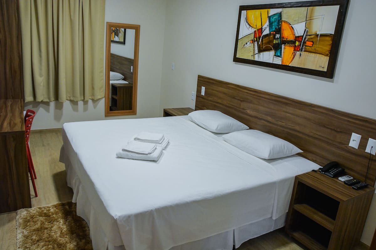 A hotel room with a large bed, a wooden headboard, a nightstand with a telephone, and a painting on the wall.