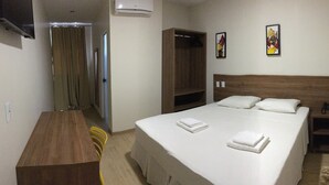 A hotel room with a bed, a wooden nightstand, a small table, and a chair. There are three paintings on the wall. - Mac Hotel (Palmas)