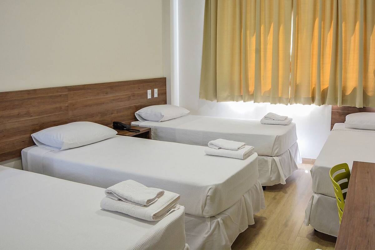 A hotel room with two single beds, a wooden headboard, a small table, and a chair.