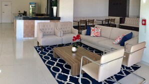 A modern living room with a sofa, coffee table, and chairs. There is a dining area with a table and chairs in the background. - Mac Hotel (Palmas)