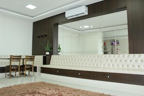 A modern living room with a white sofa, wooden chairs, a fluffy rug, and a large mirror. - Mac Hotel (Palmas)