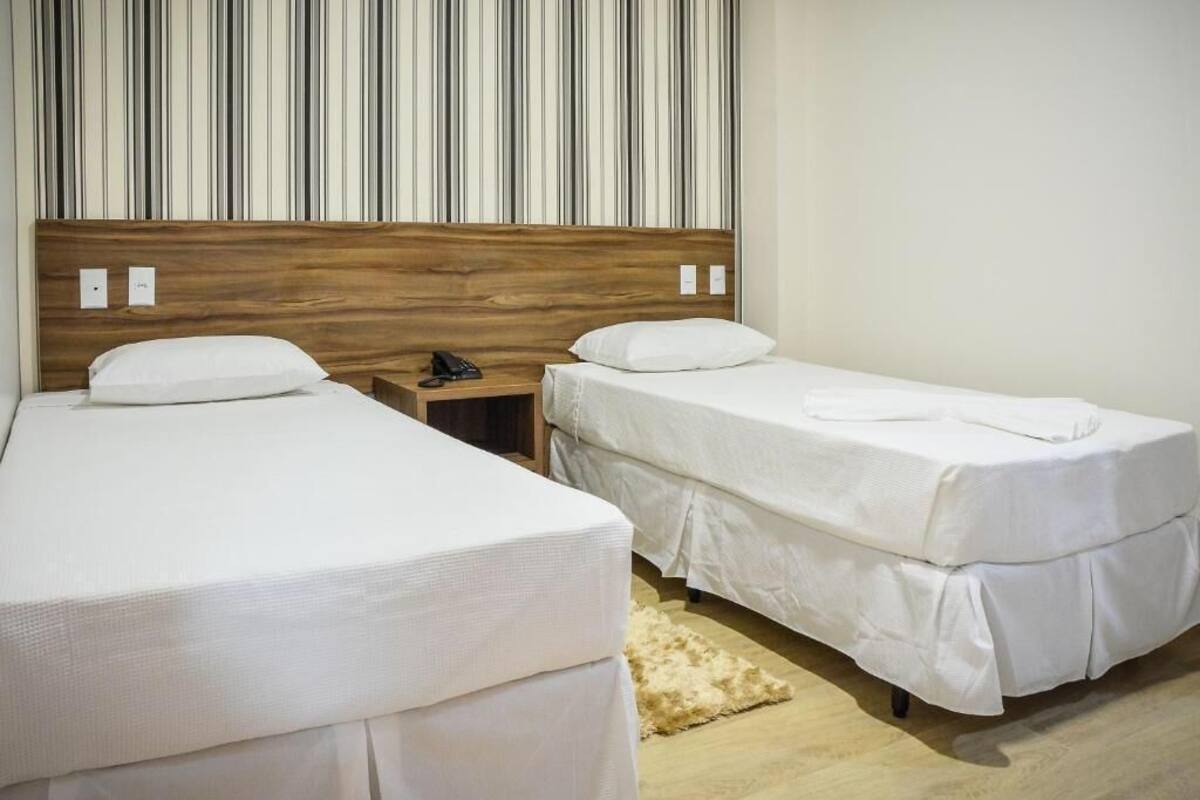 A hotel room with two single beds, a wooden headboard, a nightstand with a phone, and a striped wall.