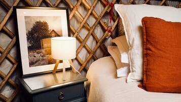 A cozy bedroom with a wooden lattice wall, a framed picture, a bedside table with a lamp, and a bed with a white and orange pillow.