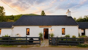 A white building with a black roof, a sign reading 'WESTER ACHRAW CROFT,' and a welcome sign. - Wester Auchraw Croft B&B (Lochearnhead)