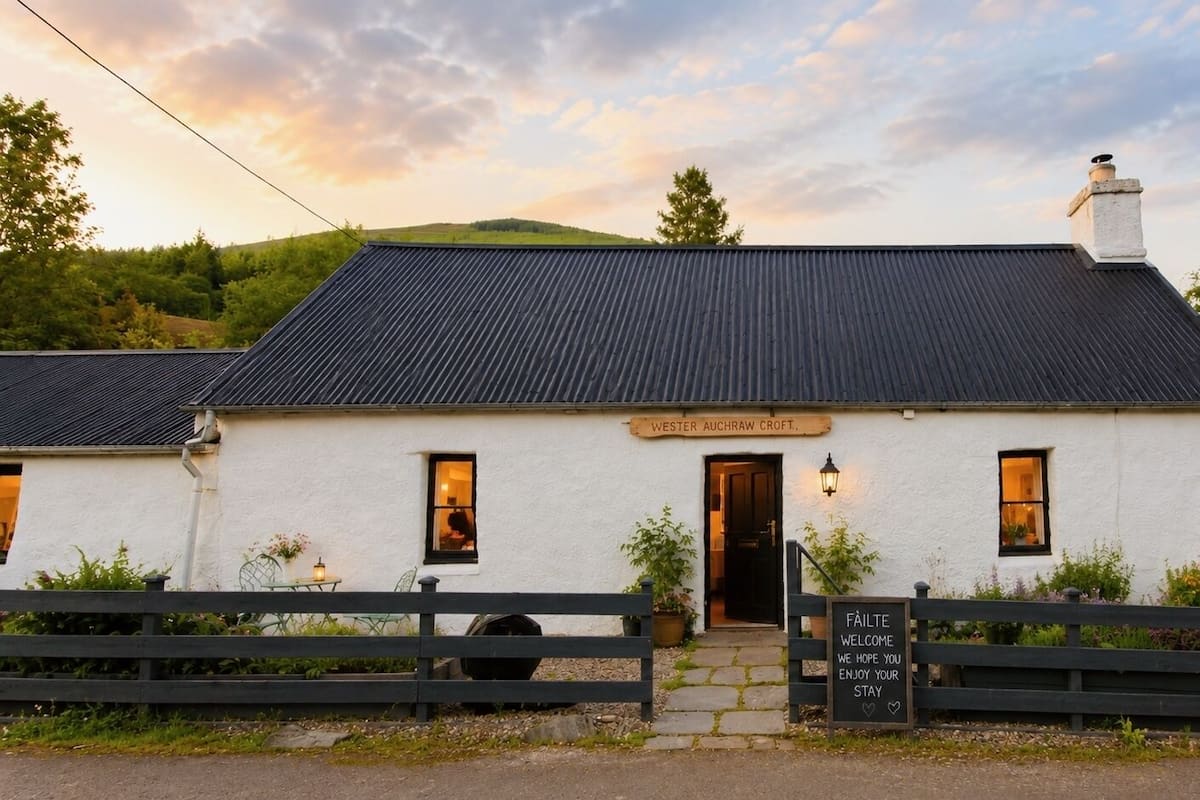 A white building with a black roof, a sign reading 'WESTER ACHRAW CROFT,' and a welcome sign.