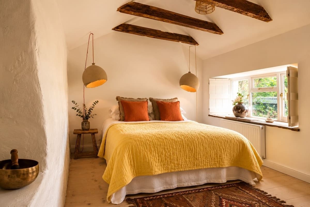 A bedroom with a bed, two hanging lamps, a window with a view, and a small table with a plant.