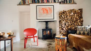Una sala de estar acogedora con un sillón rojo, un taburete pequeño, una chimenea, una estantería y un cuadro abstracto enmarcado.