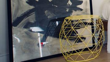 A large abstract painting with a black frame on a wall, a geometric yellow chair, and a wooden floor.