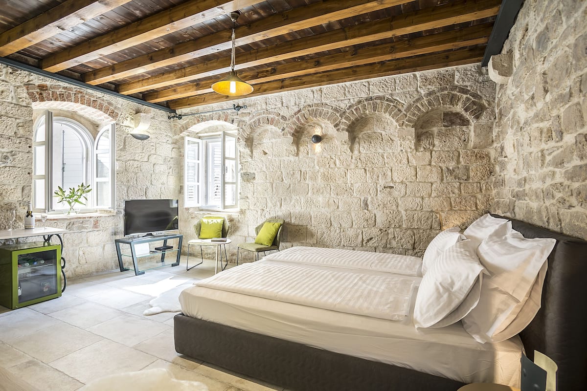 A bedroom with a stone wall, a bed, a TV, a desk, and a chair.