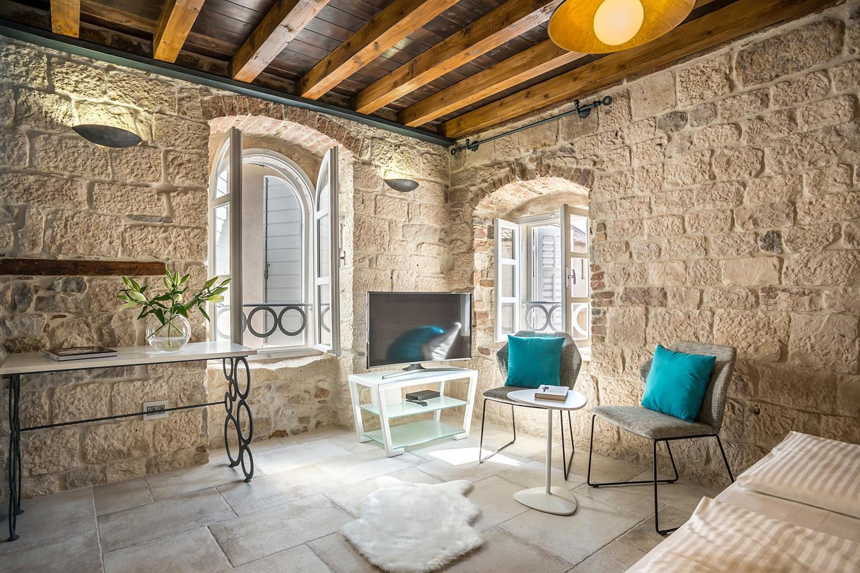 A stone-walled room with a television, two chairs, a small table, and a white rug.