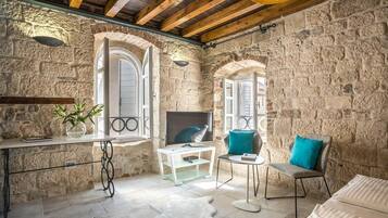 A stone-walled room with a television, two chairs, a small table, and a white rug.