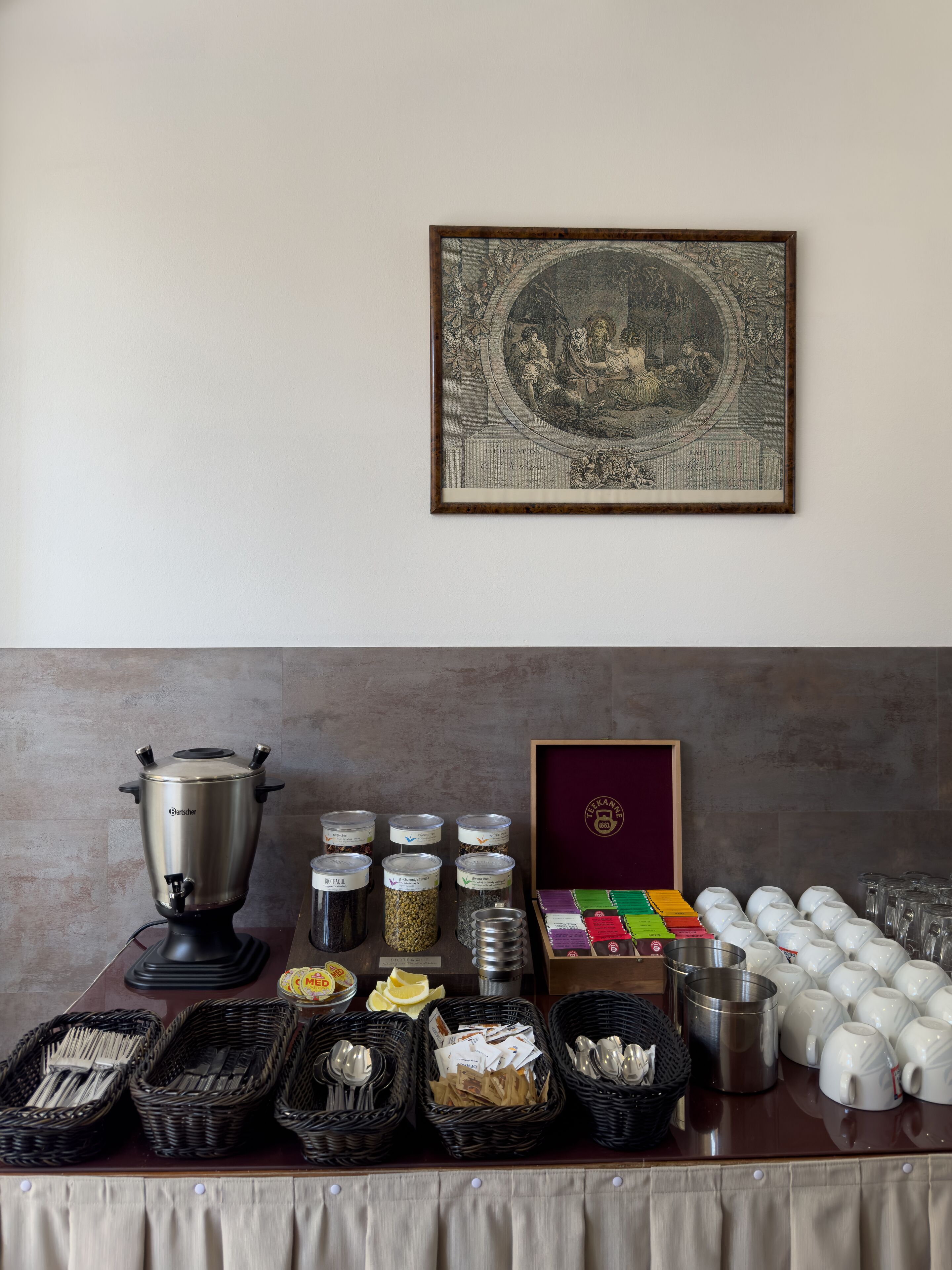 A buffet setup with various food items, utensils, and a framed artwork on the wall.