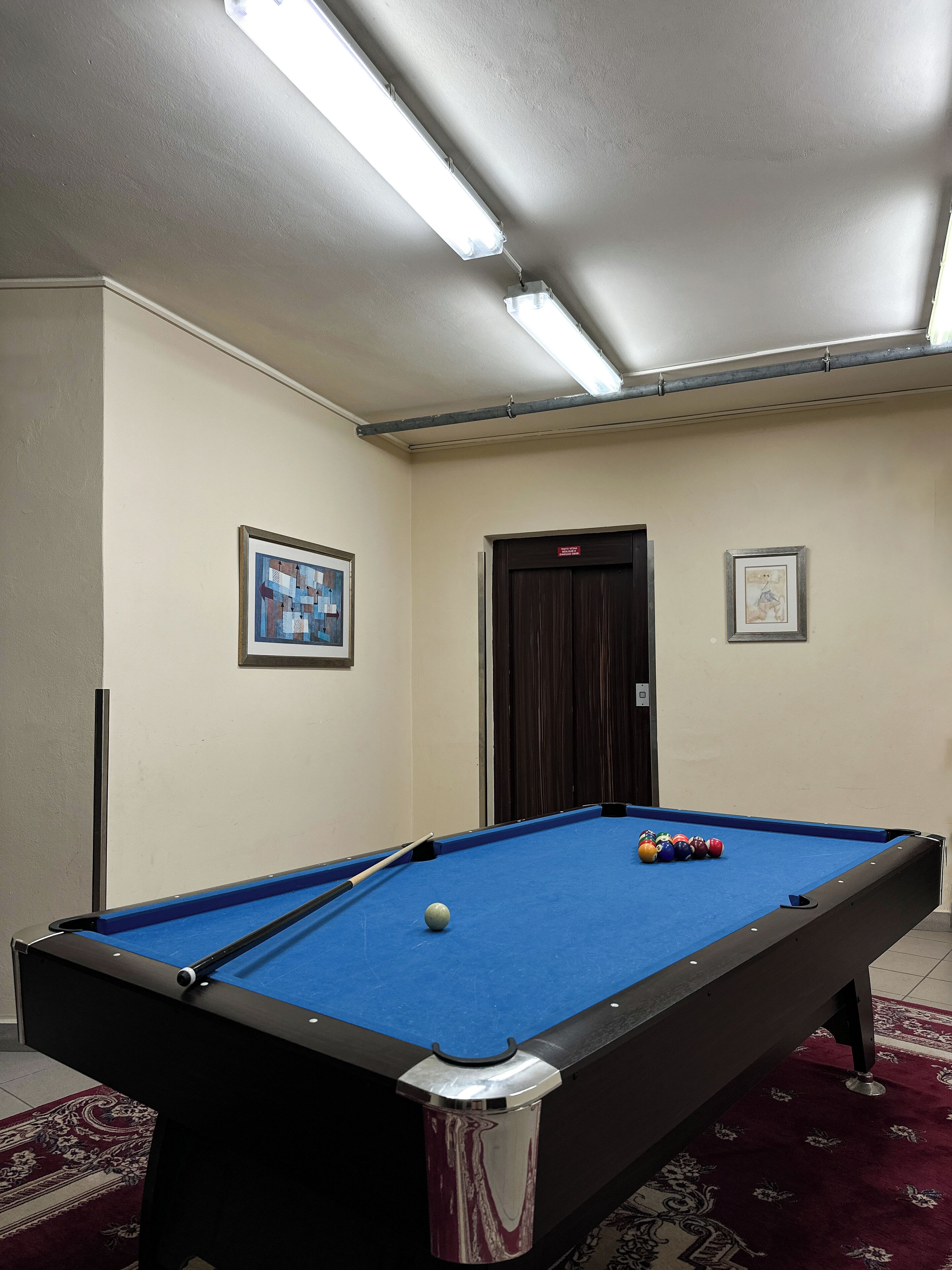 Una mesa de billar con bolas, un cuadro en la pared y una puerta con un letrero.