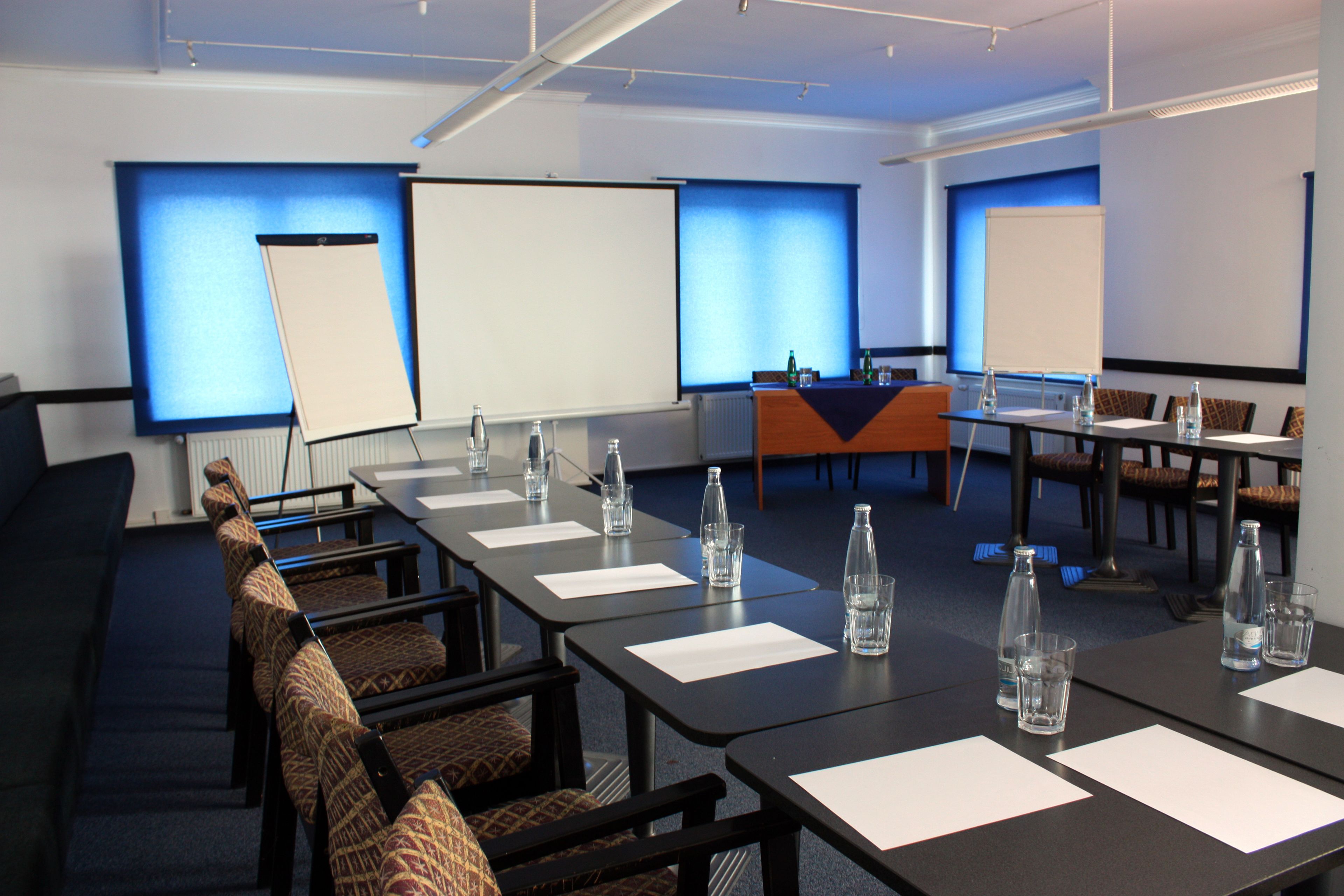 A conference room with a long table, chairs, and projection screens.