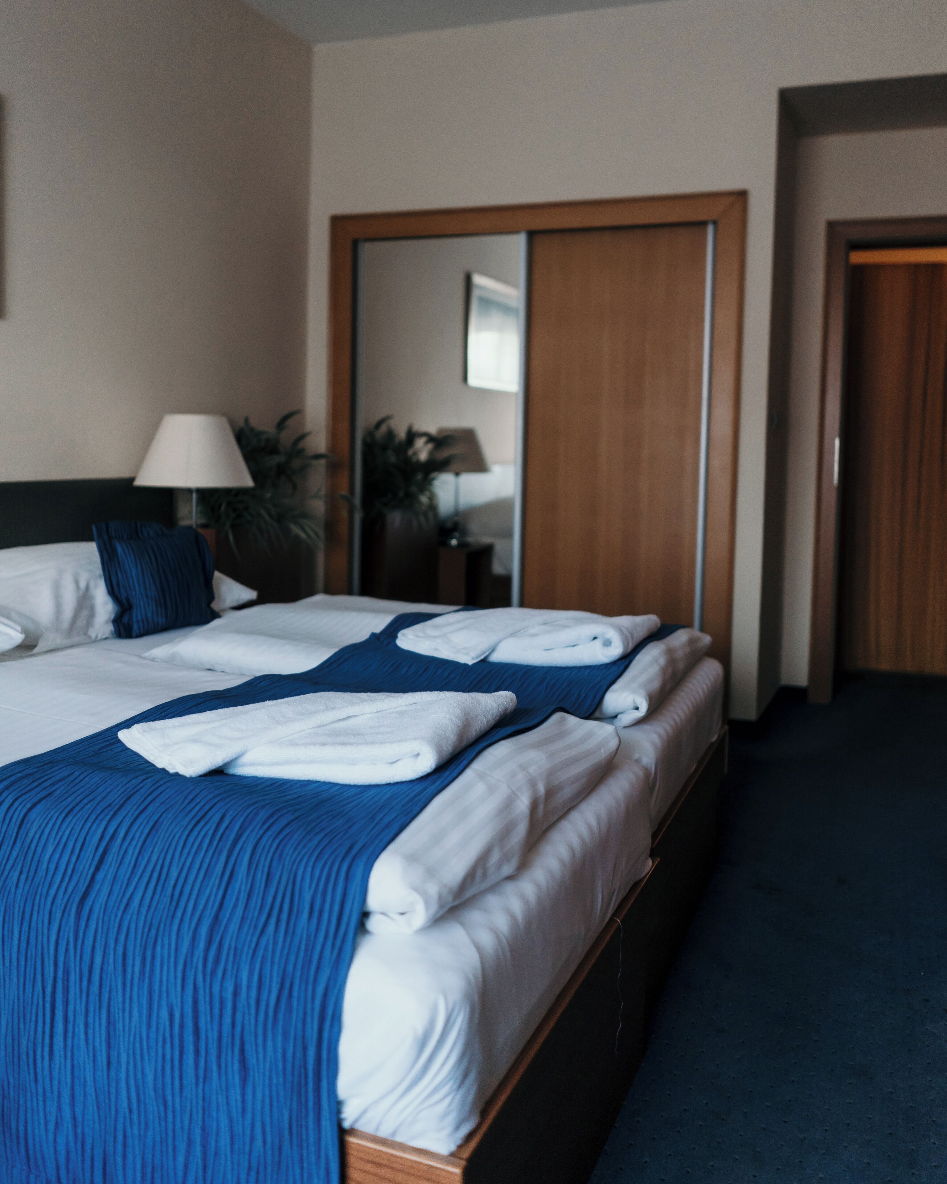 A hotel room with a neatly made bed, a wooden headboard, a mirror, and a door.