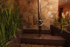 A stone wall with a metal pole in the center, surrounded by potted plants and a tiled floor. - Hotel Theresia Kolín (Kolin)