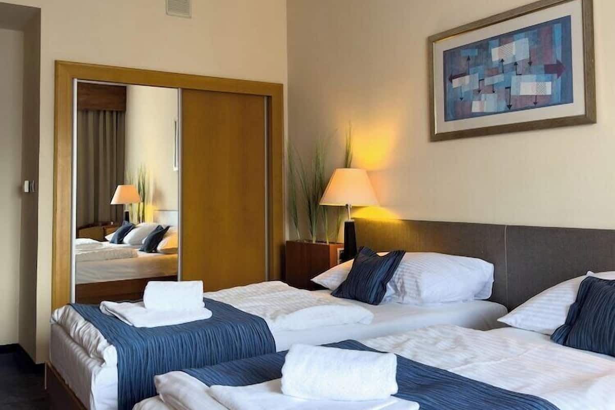 A hotel room with two beds, a mirror, a painting, and a lamp.