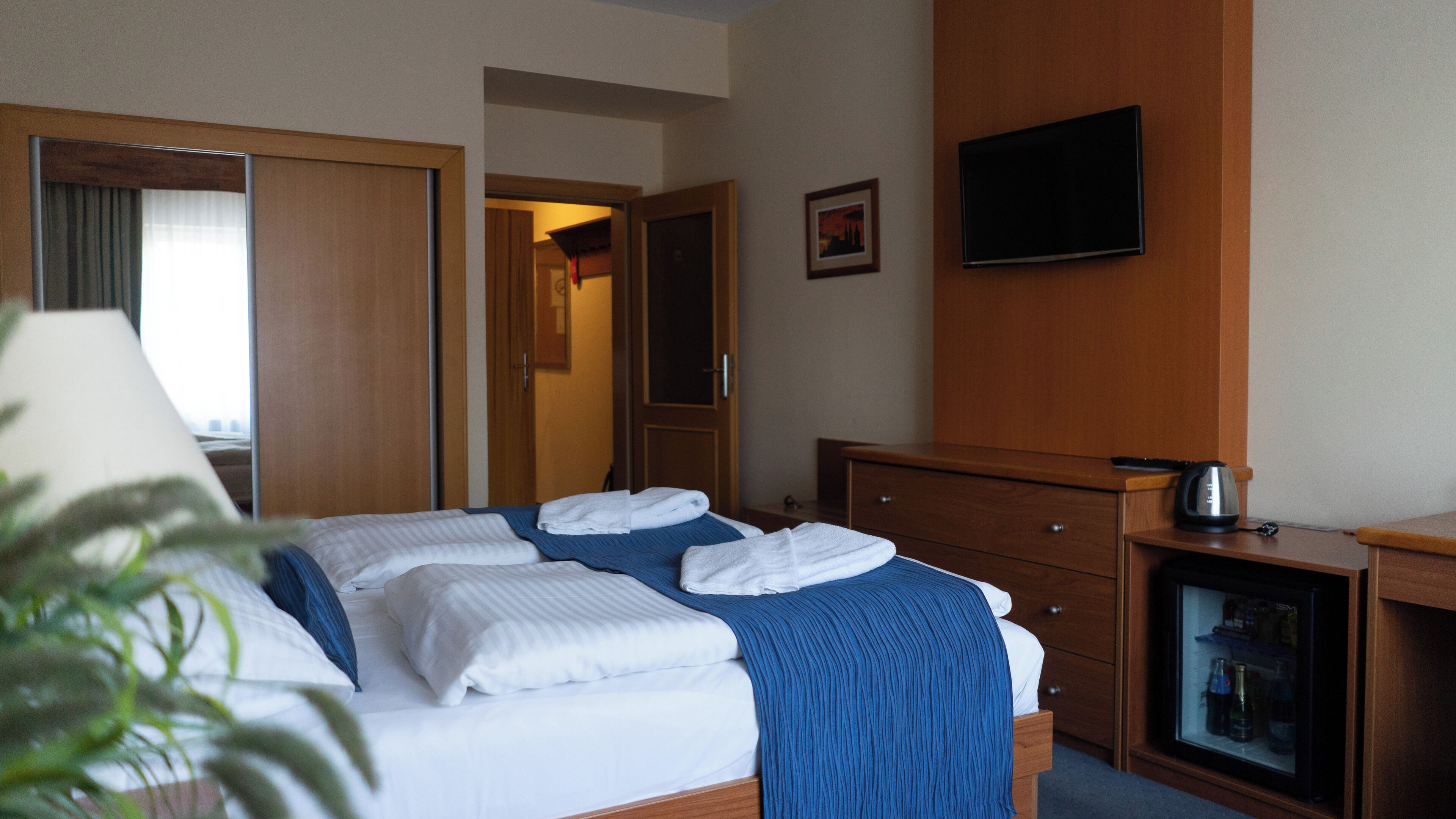 A hotel room with a bed, a television, a minibar, and a door leading to another room.